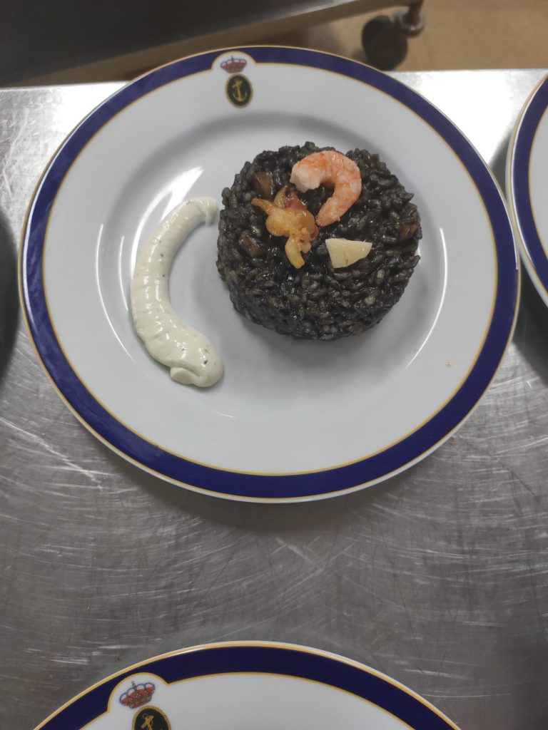 Arroz negro con mariscos y alioli servido en plato de cerámica
